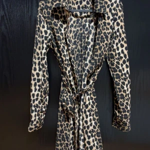 Leopardmönstrad klänning med knyt - Snygg leopardmönstrad klänning med knyt i midjan. Perfekt för att ge en djärv touch till din outfit. Långärmad och med en klassisk krage.