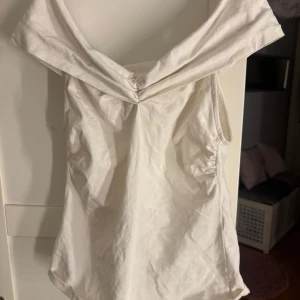 Vit ärmlös topp från Holly & Whyte - Säljer en stilren vit ärmlös topp från Holly & Whyte. Toppen har en elegant draperad krage och är perfekt för varma dagar. Tillverkad i ett mjukt och bekvämt material.