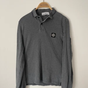 Grå halvkrage från Stone Island - Snygg grå halvkrage från Stone Island med klassisk krage och knappar. Tröjan har en broderad logotyp på bröstet och är perfekt för en stilren look. 