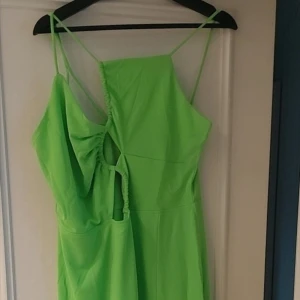 Grön långklänning med smala axelband - Snygg grön långklänning med smala axelband och en unik asymmetrisk design. Klänningen har en slits och är perfekt för sommarens festligheter. Tillverkad i ett lätt och bekvämt material.