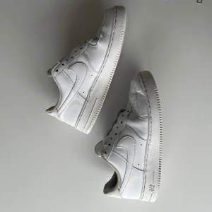 Vita Nike Air Force sneakers - Säljer ett par klassiska vita Nike Air Force sneakers. Skorna har en stilren design med snörning och den ikoniska 'AIR' loggan på sulan. Perfekta för en casual look. Sulan är inte med tyvärr men går att bara lägga in en annan sula från en annan sko!
