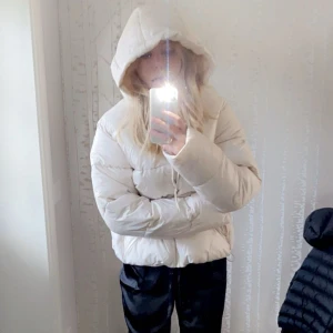 Beige pufferjacka från H&M - Säljer en snygg beige pufferjacka från H&M med huva och dragkedja. Jackan är perfekt för kyliga dagar och har en stilren design. Den är tillverkad i ett syntetmaterial med Thermolite EcoMade för extra värme. Använd 1 gång