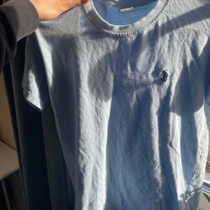 Ljusblå t-shirt från Ralph Lauren - Säljer en stilren ljusblå t-shirt från Ralph Lauren med korta ärmar och en liten broderad logga på bröstet. Perfekt för en avslappnad look. Passar bra till jeans eller shorts.