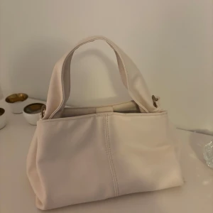 Beige handväska - Snygg beige handväska med två handtag och flera fack inuti. Perfekt för att hålla ordning på dina saker. Stilren och enkel design som passar till många tillfällen.