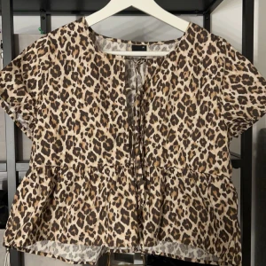 Leopardmönstrad blus från Gina Tricot - Säljer en trendig leopardmönstrad blus från Gina Tricot. Blusen har korta ärmar och en knytning framtill som ger en snygg detalj. Använd en gång💞