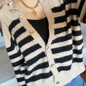 Beige och svart randig cardigan  - Säljer en mysig beige kofta med svarta ränder och knappar framtill. Perfekt för en avslappnad stil och enkel att matcha med olika outfits.