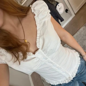 Vit blus med volangdetaljer - Vit blus med volangdetaljer och knappar framtill.