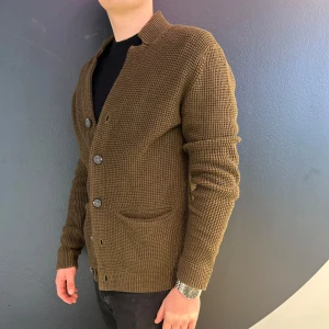 Brun stickad kofta med knappar - Snygg brun stickad kofta med knappar framtill. Den har långa ärmar och två fickor. Perfekt för kyligare dagar.