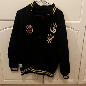 Vintage Evisu - Snygg svart zip tröja från Evisu med gula detaljer och mönster. Jackan har dragkedja och långa ärmar med ribbade muddar. Den har ett unikt tryck på ryggen och märkeslogga på framsidan. Perfekt för dig som vill sticka ut! Vintage i nice stil. Passar nån runt 170-175