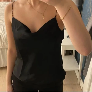 Svart satinlinne från mango  - Snyggt svart linne i satin från Mango med tunna axelband. Perfekt för en stilren look. Linnet har en elegant och enkel design som passar till många olika outfits.