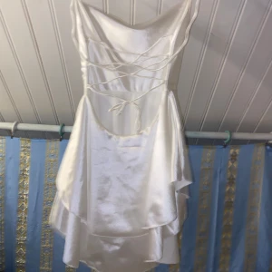 Vit siden klänning - Säljer en elegant vit klänning i satin med omlott-design och knytning i ryggen. Perfekt för speciella tillfällen med sin glänsande yta och stilrena look.