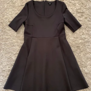 Svart klänning från COS med kort ärm - En stilren svart klänning från COS med rund halsringning och korta ärmar. Klänningen har en lätt utställd kjol och dragkedja bak. Perfekt för dig som gillar minimalistisk design och klassiska snitt.