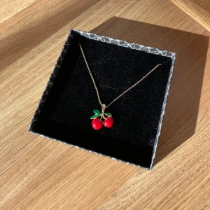 Halsband med körsbärshänge - Säljer ett gulligt halsband med ett körsbärshänge i rött och grönt. Kedjan är tunn och guldfärgad, och hänget föreställer två röda körsbär med gröna blad. Perfekt för dig som vill ha en söt detalj till din outfit! Är osäker på varifrån den är köpt men skulle gissa på Åhléns, glitter eller ur och Penn. Den är guldfärgad alltså ej äkta. På spännet har lite färg lossnat men ingen annan stans. Hör av er vid frågor!💕