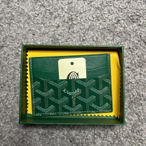 Grön korthållare från G|oyard - Säljer en snygg grön korthållare från G|oyard med deras klassiska mönster och logga framtill. Korthållaren har flera fack för kort och är tillverkad i skinn. Kommer med original ask och putsduk. Desutom med tag, 