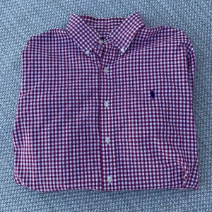 Rosavit rutig skjorta från Polo Ralph Lauren - Säljer en klassisk rosavit rutig skjorta från Polo Ralph Lauren som är helt ny endast prövad ett par gånger, skjortan är i custom fit. Skjortan har knappar hela vägen, button-down krage och lång ärm. Perfekt för dig som gillar stilrena och tidlösa plagg. Perfekt inför sommaren för dig som vill ha något snyggt och skönt på dig. Tveka inte på att höra av dig vid frågor, priset är ej spikat