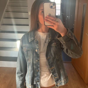 Klassisk blå jeansjacka - Säljer en klassisk blå jeansjacka med knappar framtill och två bröstfickor. Jackan har normal passform och långa ärmar. Perfekt att slänga över en t-shirt för en avslappnad look.