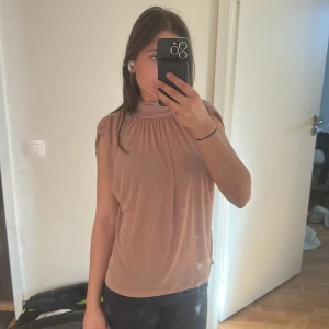Beige polotopp med rynkade axlar - Säljer en beige polotopp med korta ärmar och rynkade detaljer vid axlarna. Toppen har en lös passform och är tillverkad i ett mjukt, stretchigt material. Aldrig använd 