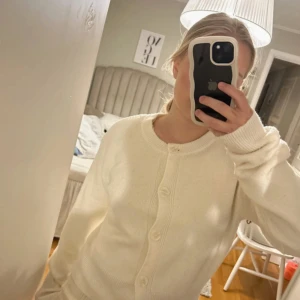 Vit croppad kofta från H&M - Säljer en supermjuk och stilren vit kofta från H&M. Koftan har långa ärmar, ribbade muddar och knappar framtill. Perfekt att slänga på sig över en topp för en enkel men snygg look.