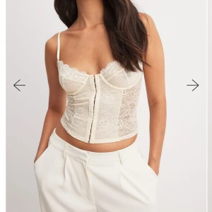 Vit spetskorsett med smala axelband - Säljer en vit korsett-topp med spetsdetaljer och smala axelband. Toppen är i spets och har knäppning framtill Stl 75 C💞 skriv för fler bilder!