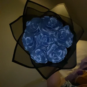 Bukett med blå rosor i svart inslagspapper - Säljer en snygg bukett med konstgjorda blå rosor, inslagna i svart transparent papper och dekorerad med ett blått band. Perfekt som present eller dekoration.