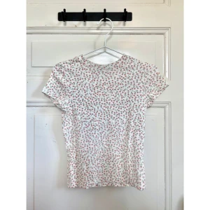 Vit blommig t-shirt - Söt vit t-shirt med små rosa blommor och gröna löv över hela tyget. ✨