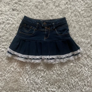 Mörkblå jeanskjol med spetskant - Lågmidjad jeanskjol omsydd från ett par jeans.  Midjemått tvärsöver- 34cm Längd-34cm