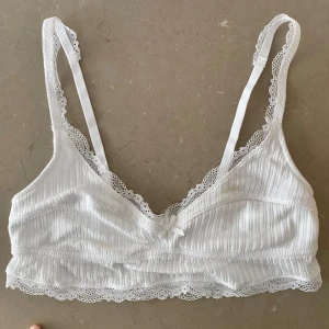 Vit pointellestickad bralette - En superfin vit pointellestickad bralette. Stretchig och med justerbara axelband. Den har tyvärr två fläckar (jag kan skicka bilder) på framsidan som fanns där när jag beställde den från Sellpy… Men jag tycker att den är för fin för att slängas..!