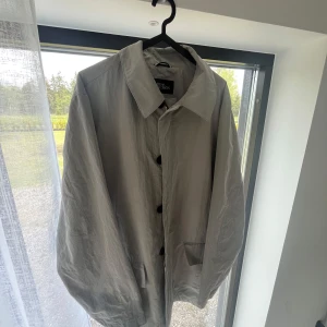 Ljusgrå rock från Oscar Jacobson - Säljer en stilren ljusgrå rock från Oscar Jacobson. Jackan har klassisk krage, knappar och dragkedja framtill samt randigt innerfoder. Perfekt för dig som vill ha en tidlös och snygg jacka till garderoben. Väldigt snygg och välskött vintage vår rock från Oscar Jacobson. Storlek 52