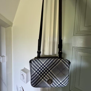 🖤🤍Rutig axelväska från Tommy Hilfiger - Säljer en snygg axelväska från Tommy Hilfiger med rutigt mönster i svart, vitt och blått. Väskan har justerbar axelrem, dragkedja upptill och TH-logga framtill. Sjukt snygg till alla årstider🙌🏼🙌🏼🙌🏼