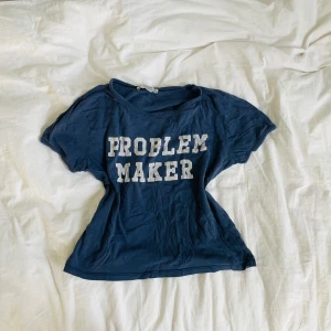 Mörkblå t-shirt med tryck - Säljer en mörkblå t-shirt med vit text 'PROBLEM MAKER' på bröstet. T-shirten har en klassisk rund halsringning och korta ärmar. Perfekt för dig som vill sticka ut med ett statement-plagg.