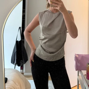 Grön ärmlös topp - Säljer en stilren grön ärmlös topp med rund halsringning. Toppen har en mjuk och något glansig yta som ger en elegant känsla. Perfekt att matcha med både jeans och kjol.