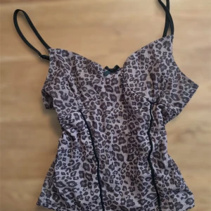 Leopardmönstrad linnetopp med svarta detaljer - Säljer en snygg leopardmönstrad linnetopp med tunna svarta axelband och svarta sömdetaljer framtill. Perfekt för dig som vill sticka ut lite extra med ett djurmönster.