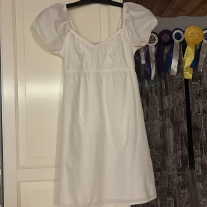 Vit kortklänning med puffärmar - Supersöt vit klänning med puffiga kortärmar och smockad rygg. Den är perfekt till avslutningen me även till annat den är använd en gång priset kan diskuteras💗💗