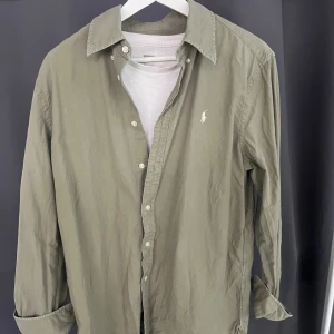 Grön Ralph Lauren Skjorta - Säljer denna utmärkta Ralph lauren skjorta då den inte har använts särskilt mycket eftersom den är lite stor på mig. Väldigt snygg ”relaxed” fit dock för sommaren. Ställ gärna frågor om det behövs och be om mer bilder också👍