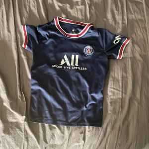 PSG fotbollströja Messi #30 - Mörkblå PSG fotbollströja med Messi och nummer 30 på ryggen. Tröjan har vita och röda detaljer vid krage och ärmslut samt klubbmärke på bröstet. Kortärmad modell med tryckta sponsorer på bröst och ärm.