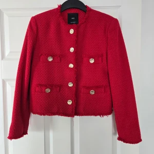 Röd kavajjacka från MNG - Säljer en snygg röd kavajjacka från MNG med guldknappar framtill och dekorativa fickor. Jackan har en rak, croppad passform och är tillverkad i ett strukturerat tyg med råa kanter. Perfekt för att lyfta vilken outfit som helst. Helt ny/aldrig använd.