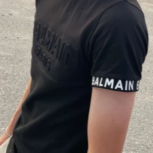 Svart t-shirt från Balmain - Säljer en svart t-shirt från Balmain med upphöjd logga på bröstet och tryckt Balmain-text på ärmslutet. Klassisk passform och rund halsringning. Perfekt för dig som gillar stilrena märkesplagg. Storlek xs
