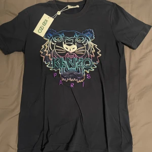 Svart t-shirt med broderad tiger från Kenzo - Svart t-shirt från Kenzo med ikonisk broderad tiger i flera färger och texten 'KENZO PARIS' framtill. T-shirten har rund halsringning och är i mjuk bomull. Perfekt för dig som vill sticka ut med en färgstark detalj. Aldrig använt.