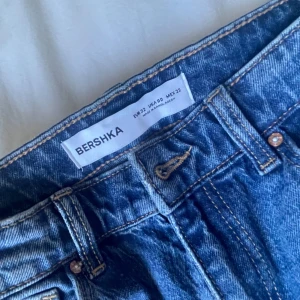Blå jeans från Bershka - Säljer ett par klassiska blå jeans från Bershka med fem fickor och gylf med dragkedja. Jeansen har en normal passform och raka ben, perfekta till vardags. Tidlös modell som är enkel att matcha med olika stilar.
