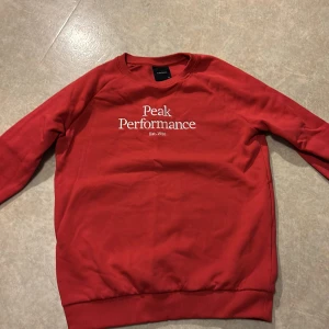 Röd sweatshirt från Peak Performance - Säljer en röd sweatshirt från Peak Performance med vit logga på bröstet. Tröjan har rund halsringning, långa ärmar och ribbade muddar vid ärmslut och nederkant. Perfekt för en avslappnad stil.
