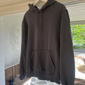 Mörkgrå hoodie med ficka - Säljer en enkel och stilren mörkgrå hoodie med huva och dragsko. Tröjan har en stor magficka och ribbade muddar vid ärmslut och nederkant. Perfekt för en avslappnad look. Storlek S