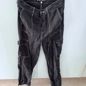 Svarta cargopants från Stay med vita sömmar - Svarta cargopants från Stay med kontrasterande vita sömmar och flera fickor på benen. Byxorna har normal passform och stängs med knapp och dragkedja. Perfekta för en avslappnad och trendig stil.