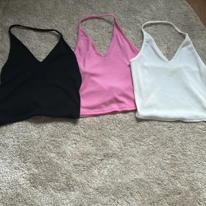 3-pack ribbade croppade linne-toppar från SHEIN - Säljer tre croppade linne-toppar från SHEIN i färgerna svart, rosa och vit. Alla toppar har v-ringning och smala axelband. Materialet är ribbat och stretchigt, perfekt för sommaren.
