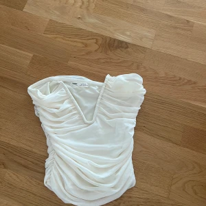 Vit omlott topp från Pull&Bear - Säljer en vit omlott topp från Pull&Bear i storlek S. Toppen har v-ringning, ärmlös design och är sydd i ett tunt, lätt material med draperade detaljer framtill🩷
