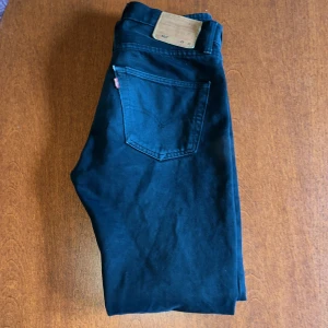 Svarta Levis 501 jeans - Klassiska svarta Levis 501 jeans med raka ben och femficksdesign. Byxorna har knappgylf och Levis ikoniska läderpatch bak i midjan. Perfekta för en stilren och tidlös look. Pris kan diskuteras 