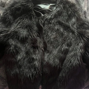 Svart fuskpälsjacka från Gina Tricot - Säljer en svart fuskpälsjacka från Gina Tricot i storlek M. Jackan har lång ärm och är helsvart med mjuk, fluffig pälsimitation. Perfekt för att ge en lyxig känsla till din outfit.