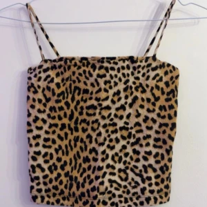 Leopardmönstrad croppad linnetopp - Säljer en croppad linnetopp med leopardmönster och tunna axelband. Toppen har en beige bas med svarta och bruna fläckar. Perfekt för dig som vill sticka ut med ett djuriskt mönster. Lappen är borta men det är en S 