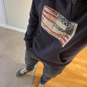 Mörkblå hoodie från Ralph Lauren - Säljer en mörkblå hoodie från Denim & Supply Ralph Lauren med en stor amerikansk flagga i tyg framtill. Tröjan har huva med knytning och en klassisk känguruficka. Perfekt för dig som gillar streetwear och vill ha något med lite edge!                Modell är 177 cm och 68 kg                                            Skriv om ni har några frågor! 🤗