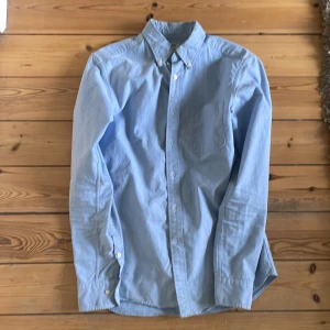 Ljusblå skjorta med button-down krage - Säljer en ljusblå skjorta i slim fit-modell med button-down krage och bröstficka. Skjortan har långa ärmar och knäppning framtill. Perfekt för dig som gillar en klassisk och stilren look.