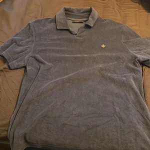 Blå pikétröja från Morris - Säljer en blå pikétröja från Morris i mjukt material. Tröjan har klassisk krage och liten broderad logga på bröstet. Perfekt för en avslappnad men ändå stilren look.